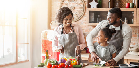 African american man teaching daughter how to cut vegetables, mom making salad, talking while cooking in kitchen, free space