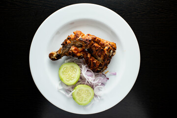 Spicy bbq Chicken Leg Piece Tikka with cucumber and onion salad served in dish isolated dark background top view of indian spices, bangladeshi and pakistani food