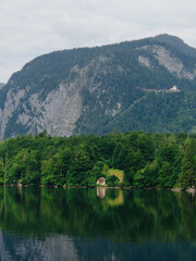 Obraz premium Small wooden house reflecting on lake with mountains in background