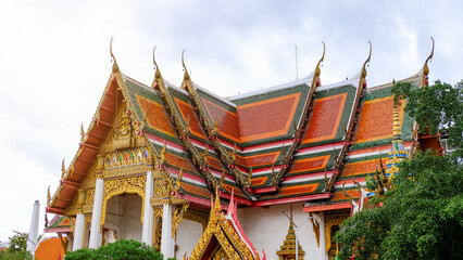 Fototapeta premium A stunning view of a traditional Thai temple adorned with vibrant colors and intricate architecture under a cloudy sky.