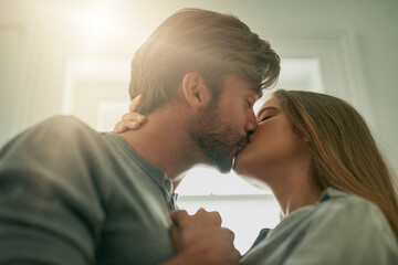 Love, couple and kiss in home for care, connection or bonding together in low angle. Man, woman and lips touch for romance, intimacy and celebrate anniversary at apartment with lens flare in profile