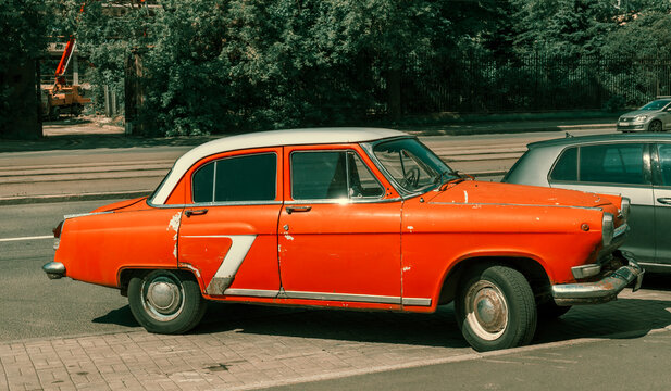 An old orange car is parked on the side of the road