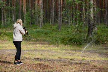 A young girl shoots from air rifle at lemonade jars in nature on a summer day. Back view.