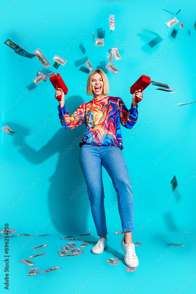 Sticker Full length vertical photo of overjoyed cool girl dressed print shirt jeans shooting money with guns isolated on blue color background