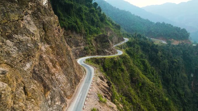 Aerial view of a dangerous winding road along a lush green mountain cliff leading to the Ha Giang Loop in Vietnam