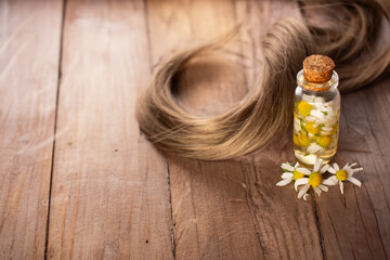 Fresh chamomile flowers, bottle with chamomile essential oil and hair on wooden background. Hair treatment concept. 
