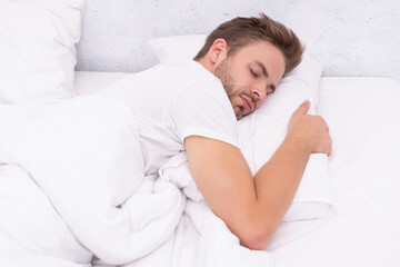 Young man sleeping or napping at home in bed at white bedroom