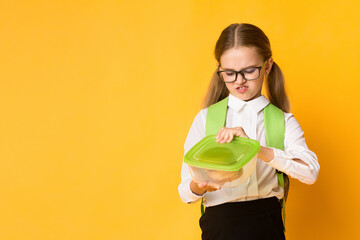 Disgusted Schoolgirl Looking At Sandwich In Lunchbox Over Yellow Studio Background. School Lunch And Gluten Intolerance. Copy Space