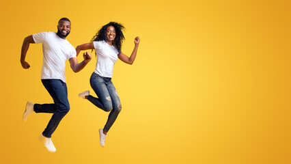 Joyful African American Man And Woman Are Running In The Air, yellow background