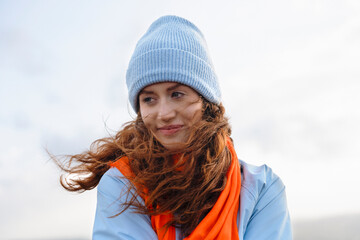 Woman With Red Hair Wearing Blue Hat and Orange Scarf Outside on Windy Day