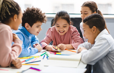 Technology And Pupils Concept. Group of excited multicultural happy junior children sitting at...