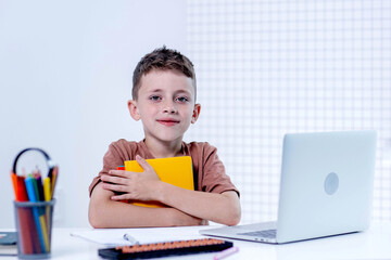 Smart schoolboy is ready to study at a neat table in a white interior.