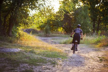 A cyclist on a mountain bike rides in the forest at sunset. Bokeh of the setting sun. Full length portrait from the back.