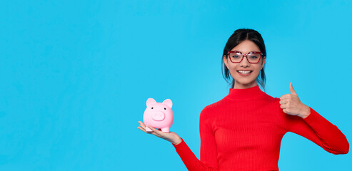 Woman Holding Pink Piggy Bank and Giving Thumbs Up Against Blue Background