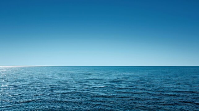 Calm, deep blue ocean water is meeting a clear sky at the horizon on a sunny day, ideal for backgrounds about nature, travel, and relaxation