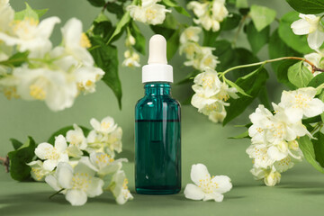 Essential oil in bottle and beautiful jasmine flowers on pale green background