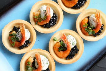 Delicious canapes with shrimps and black caviar on table, top view