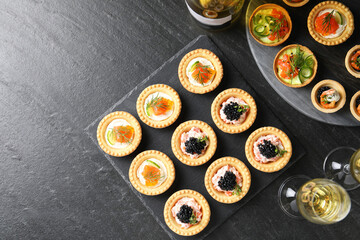 Delicious canapes and glasses of white wine on black textured table, flat lay. Space for text