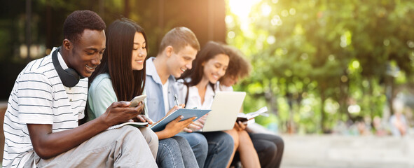 Multiethnic students having fun, studying together for exams outdoors in campus, chatting and smiling during break in classes