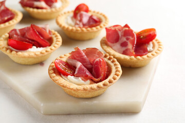 Delicious canapes with jamon, cream cheese and cherry tomatoes on light table, closeup