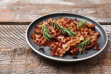 Slices of tasty fried bacon, peppercorns and rosemary on wooden table