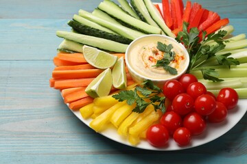 Tasty homemade hummus and different vegetables served on light blue wooden table, closeup
