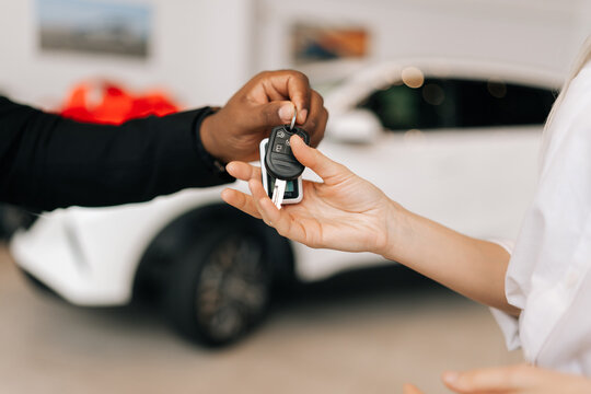 Closeup side view of unrecognizable female buyer getting car key and congratulation from black auto dealer male buying new auto in dealership. Woman car owner during handing over keys at showroom.