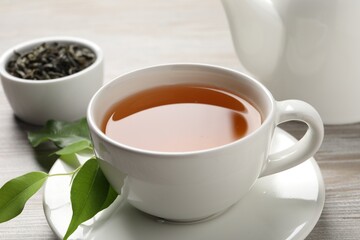 Refreshing green tea in cup and leaves on grey wooden table, closeup