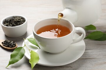 Pouring refreshing green tea into cup at grey wooden table, closeup
