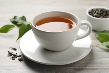 Refreshing green tea in cup and leaves on grey wooden table, closeup