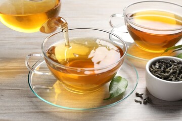 Pouring refreshing green tea into cup at grey wooden table, closeup
