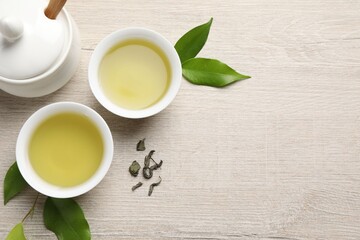 Refreshing green tea in cups, sugar bowl and leaves on wooden table, flat lay. Space for text