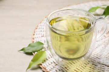 Refreshing green tea in cup and leaves on wooden table, closeup. Space for text