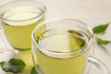 Refreshing green tea in cups and leaves on wooden table, closeup