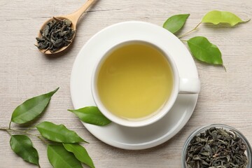Refreshing green tea in cup, spoon and leaves on wooden table, flat lay