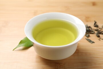 Refreshing green tea in cup and leaves on wooden table, closeup