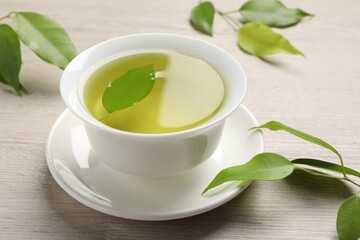 Refreshing green tea in cup and leaves on wooden table, closeup