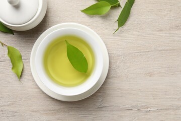 Refreshing green tea in cup, sugar bowl and leaves on wooden table, flat lay. Space for text