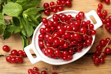 Fresh red currants in bowl and mint on wooden table, flat lay