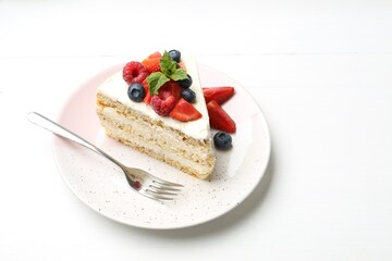 Tasty sponge cake with fresh berries and mint served on white table. Space for text