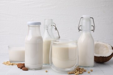 Different types of vegan milk and ingredients on white tiled table