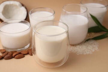 Different types of vegan milk and ingredients on beige table, closeup