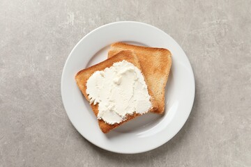 Delicious toasted bread slices with cream cheese on grey textured table, top view