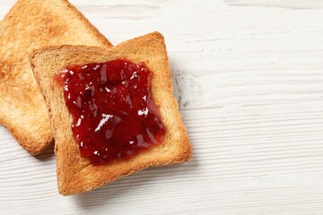 Delicious toasted bread slices with jam on white wooden table, top view. Space for text