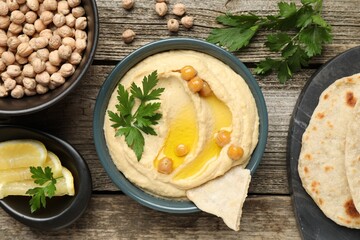 Delicious hummus with olive oil, chickpeas, lemon and pita on wooden table, flat lay