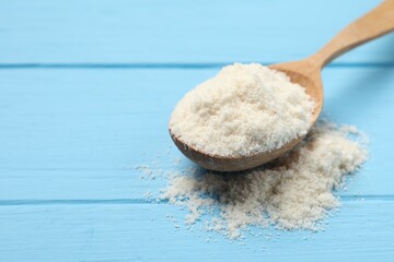 Fresh coconut flour in spoon on light blue wooden table, closeup. Space for text