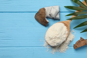 Fresh coconut flour in spoon, nut and palm leaf on light blue wooden table, flat lay. Space for text
