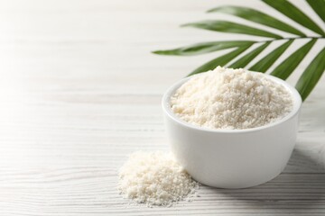 Fresh coconut flour in bowl and palm leaf on white wooden table, space for text