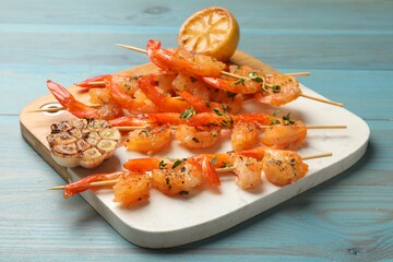 Delicious grilled shrimp skewers, lemon and garlic on light blue wooden table, closeup
