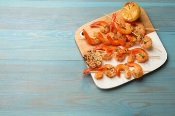 Delicious grilled shrimp skewers, lemon and garlic on light blue wooden table, top view. Space for text